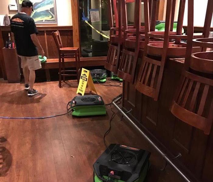 Green air movers on wood flooring near a table with chairs stacked on top.