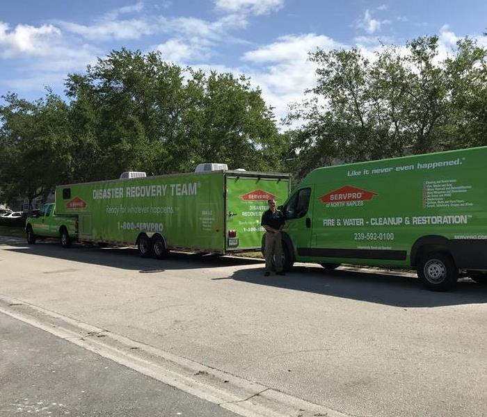 Two green SERVPRO vehicles parked outside near trees.