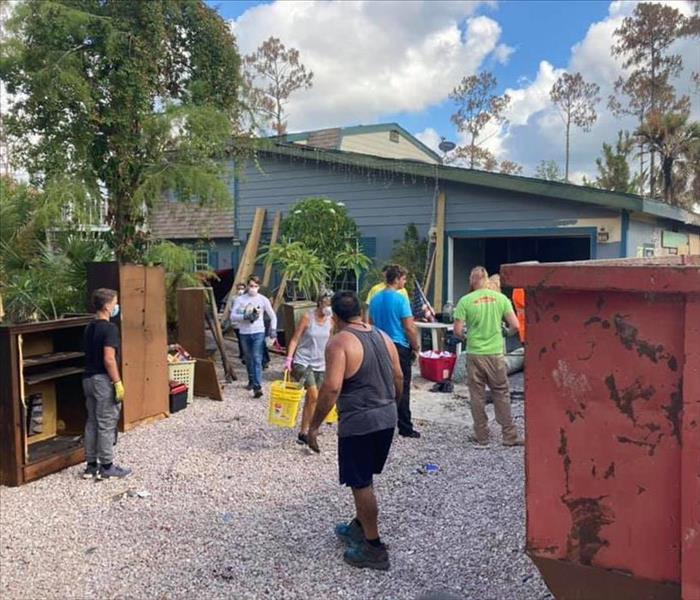 A group of people standing outside of a home with lots of debris and tools.